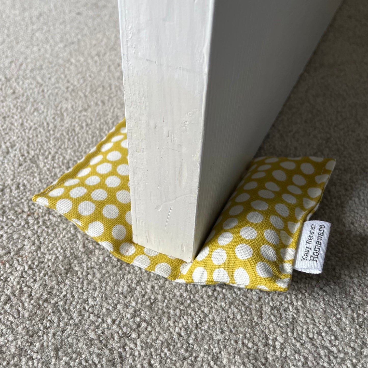 Yellow polka dot fabric door wedge with a white label on a gray carpet