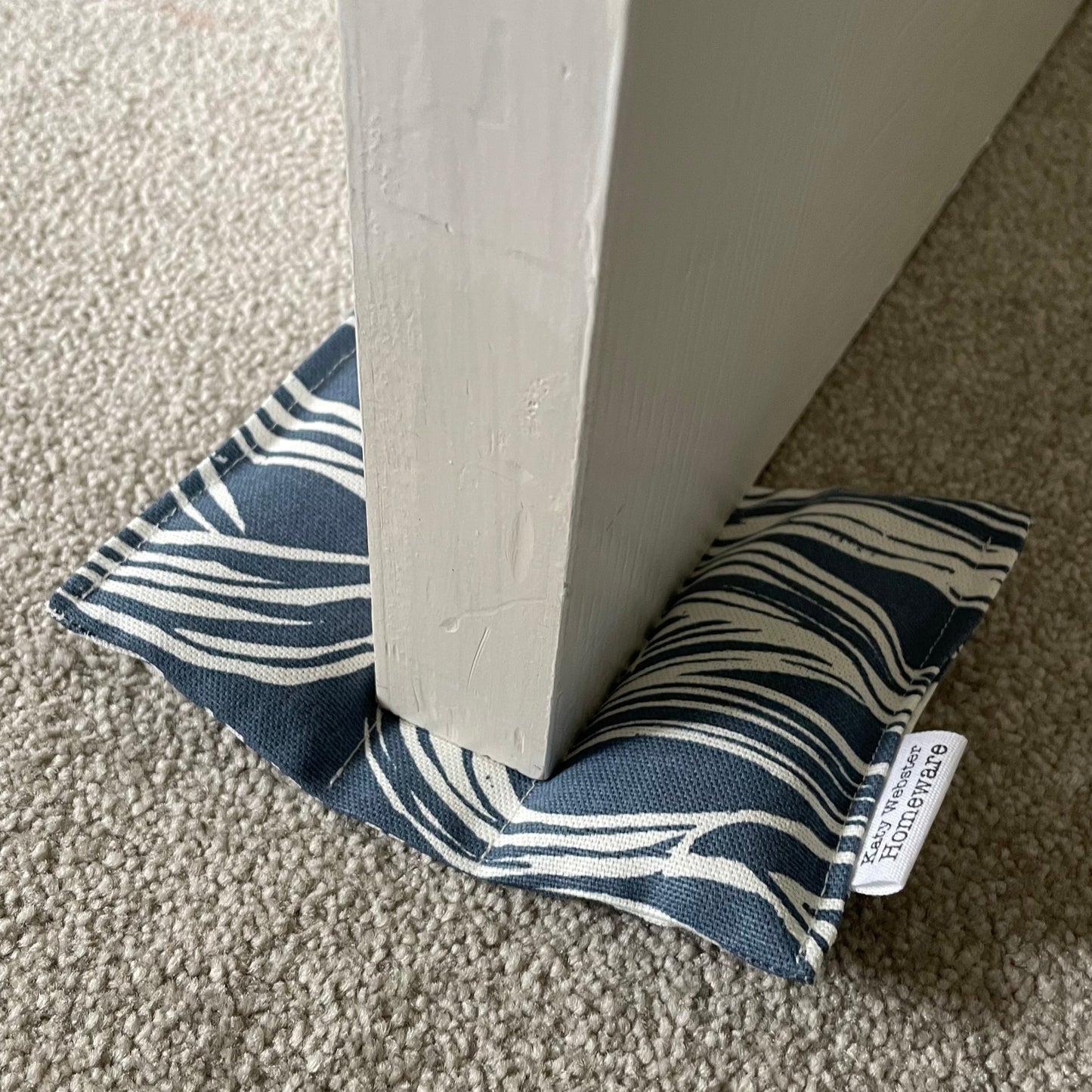 Sea surf fabric door wedge on a grey carpet.