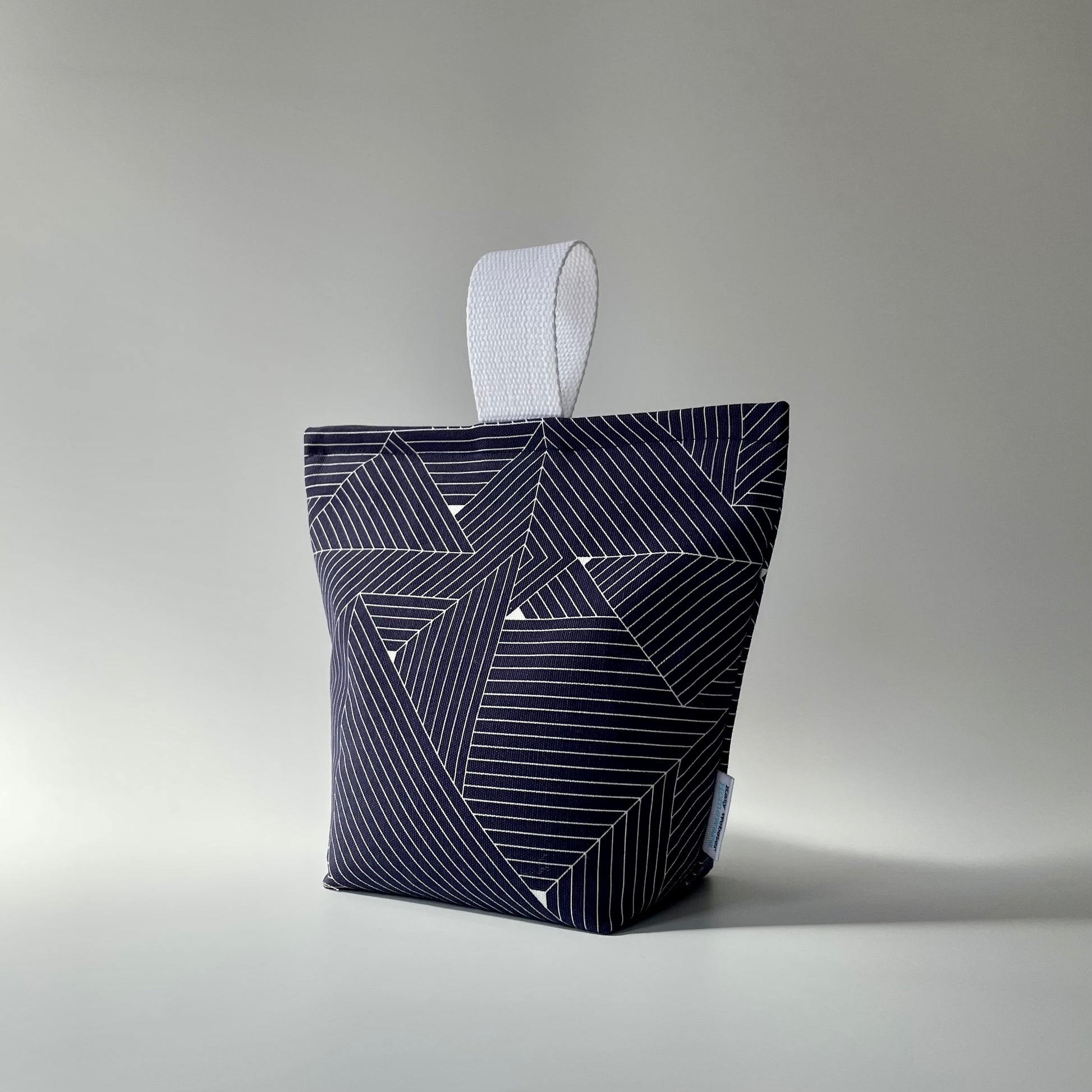 Navy blue and white grid patterned fabric doorstop with white webbed handle on top.