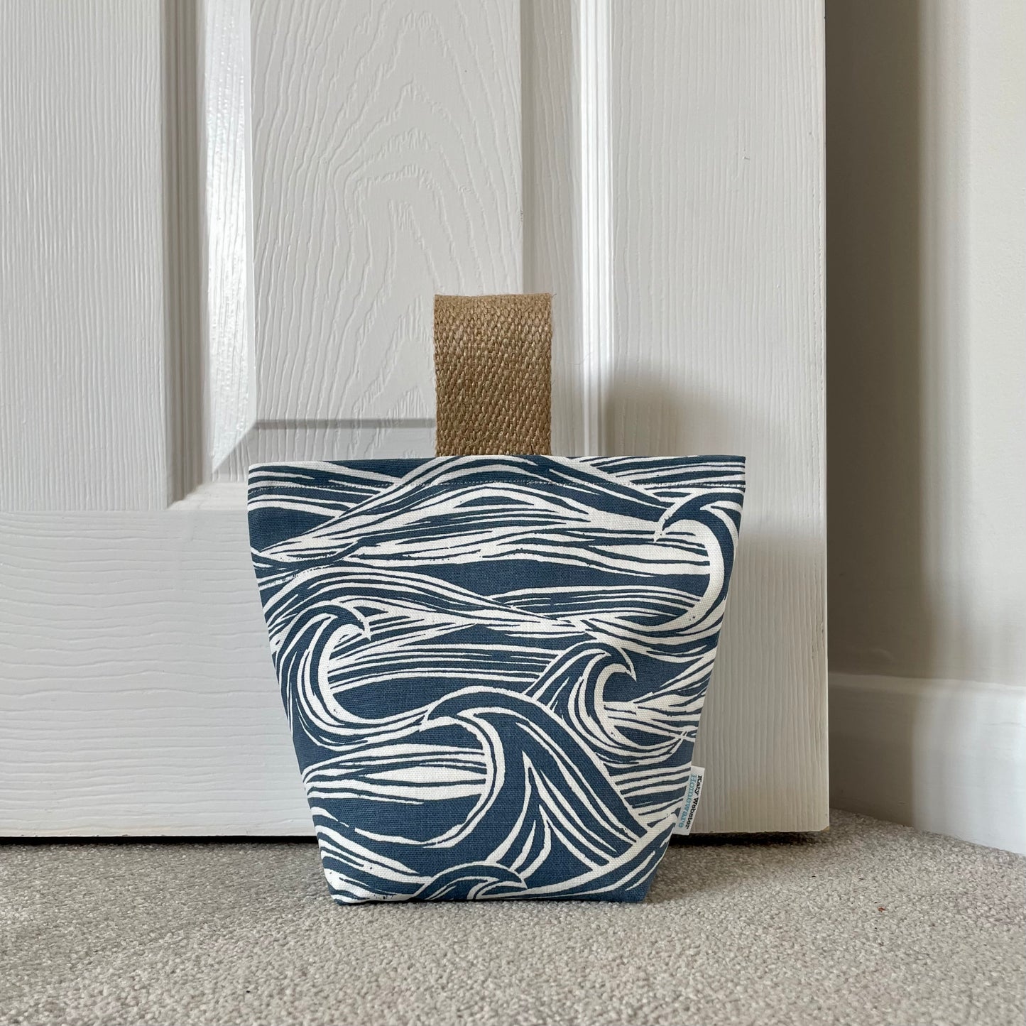 Wave print fabric doorstop with jute handle shown against door.