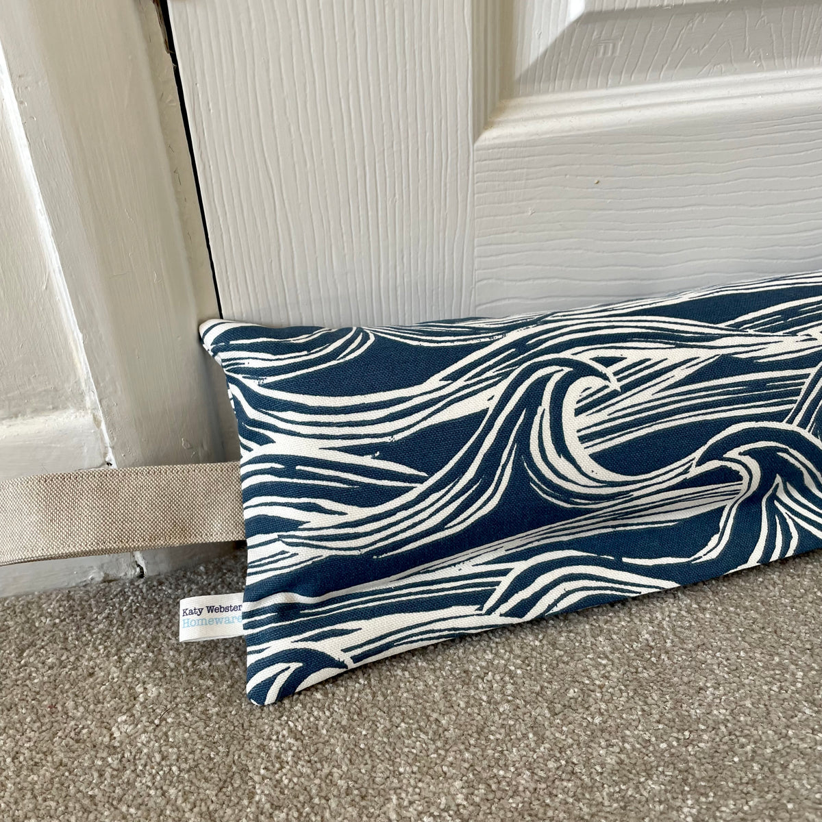 Navy and white wave-patterned weighted draught excluder against a white door.