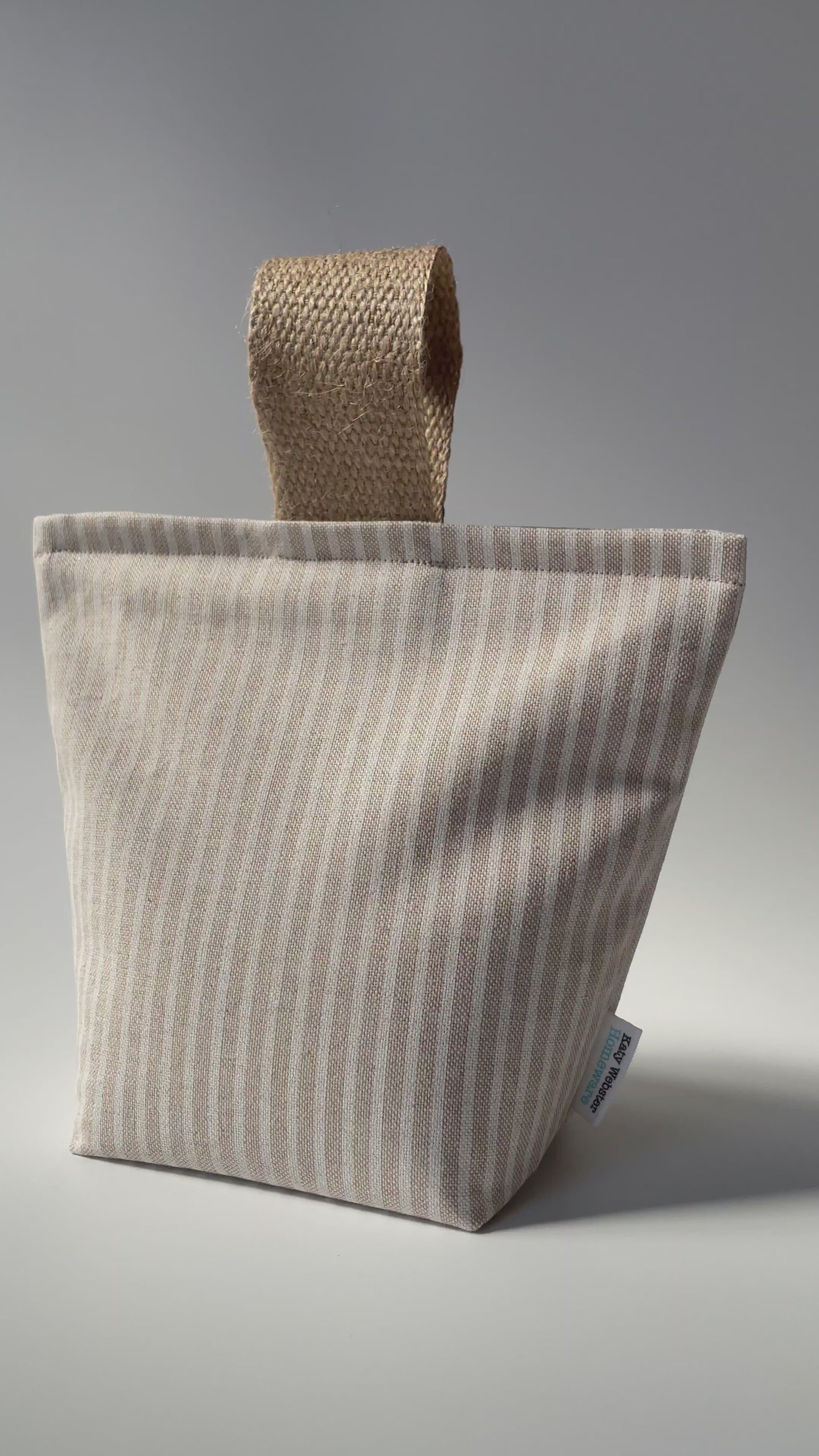 Overview of fabric doorstop with a beige and white vertical pinstripe pattern, featuring a thick jute handle on top.