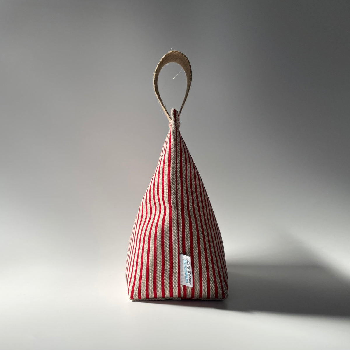 Red and beige stripe fabric doorstop with thick jute handle on top.