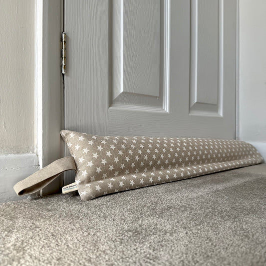 A fabric draught excluder with a beige and white star pattern rests on a carpeted floor in front of a closed panelled door.
