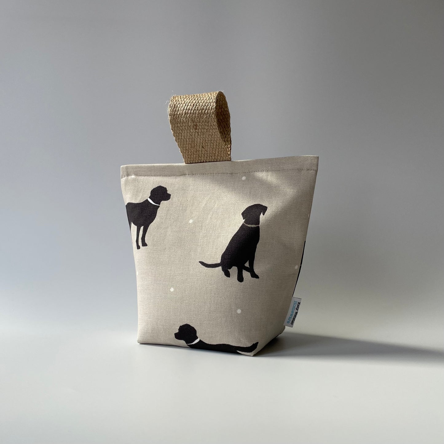 Black Lab print on taupe background with white dots fabric doorstop. Thick jute handle on top.