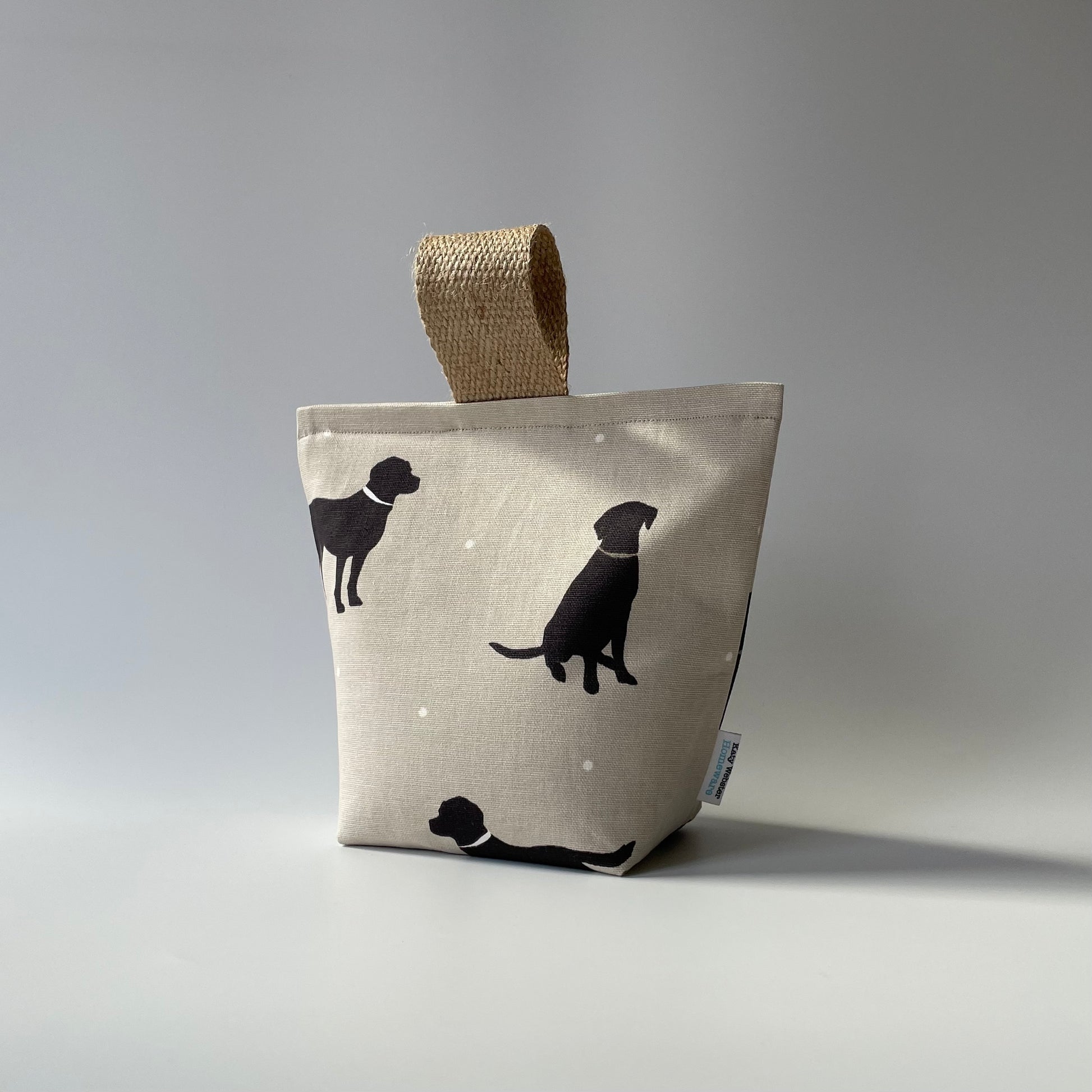 Black Lab print on taupe background with white dots fabric doorstop. Thick jute handle on top.