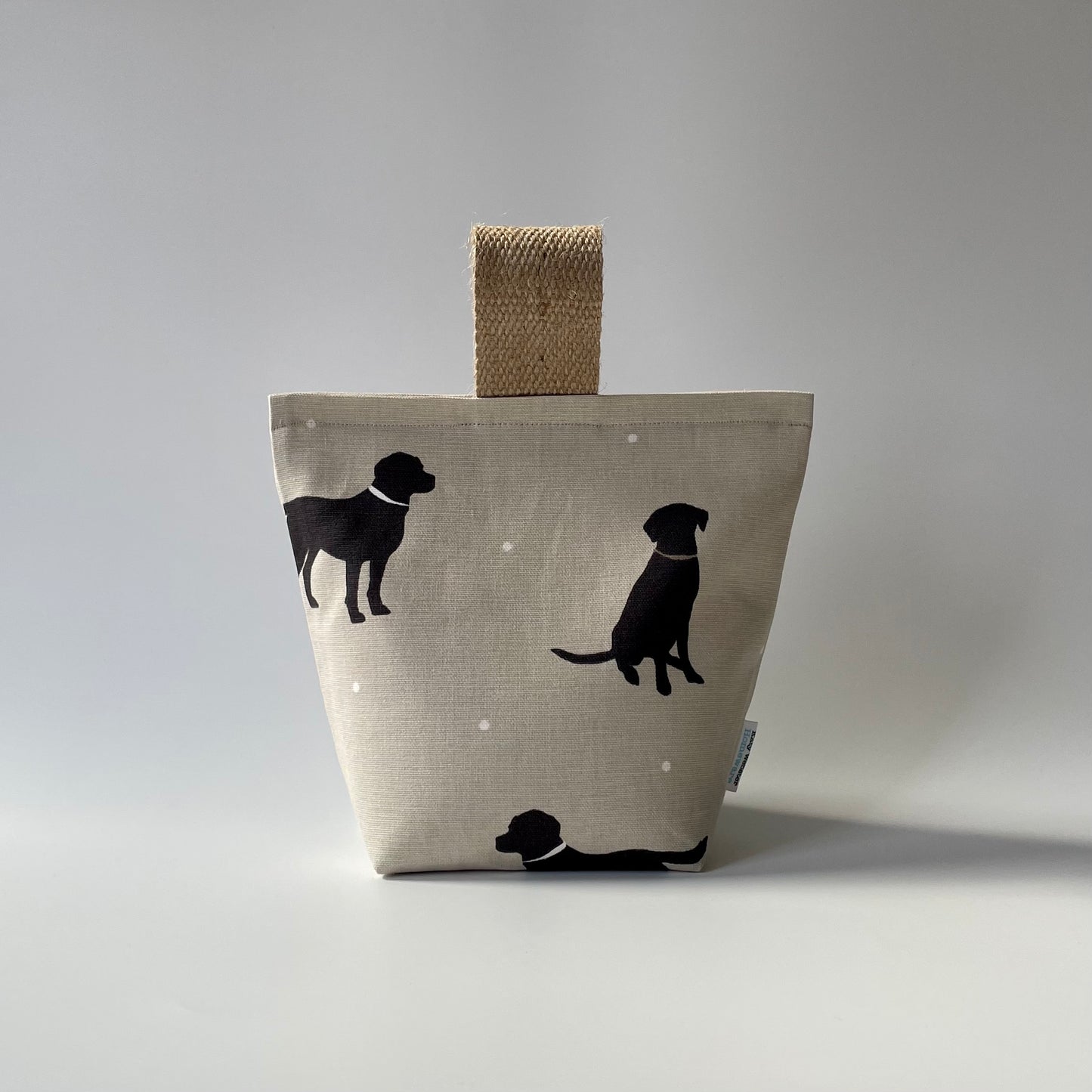 Black Lab print on taupe background with white dots fabric doorstop. Thick jute handle on top. 