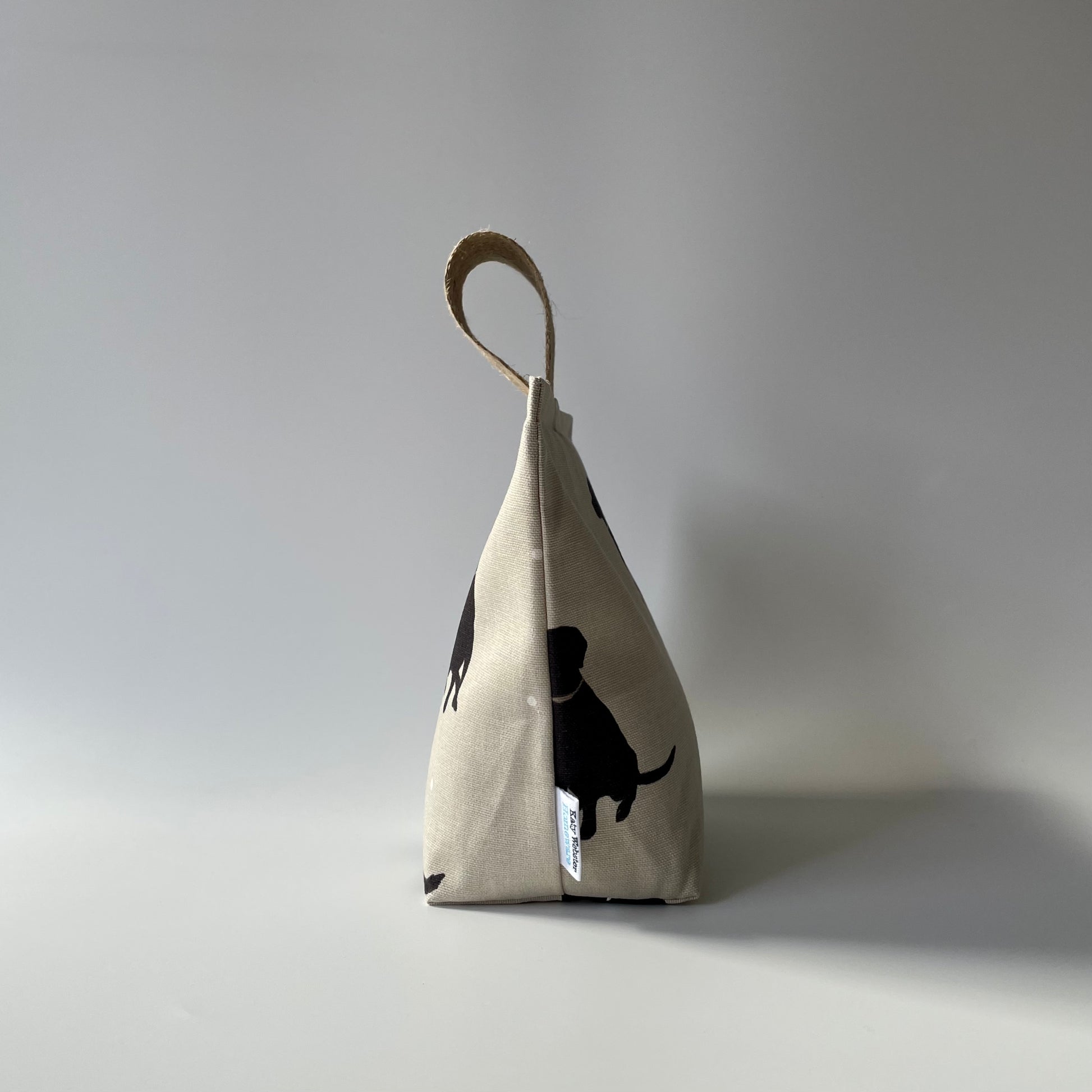 Black Lab print on taupe background with white dots fabric doorstop. Thick jute handle on top.