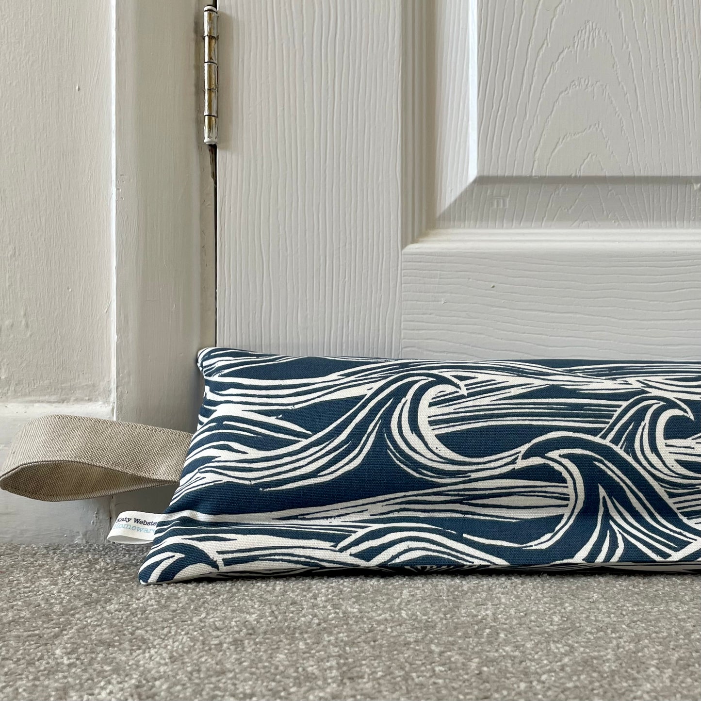Navy and white wave-patterned draught excluder on a carpet floor next to a closed door.