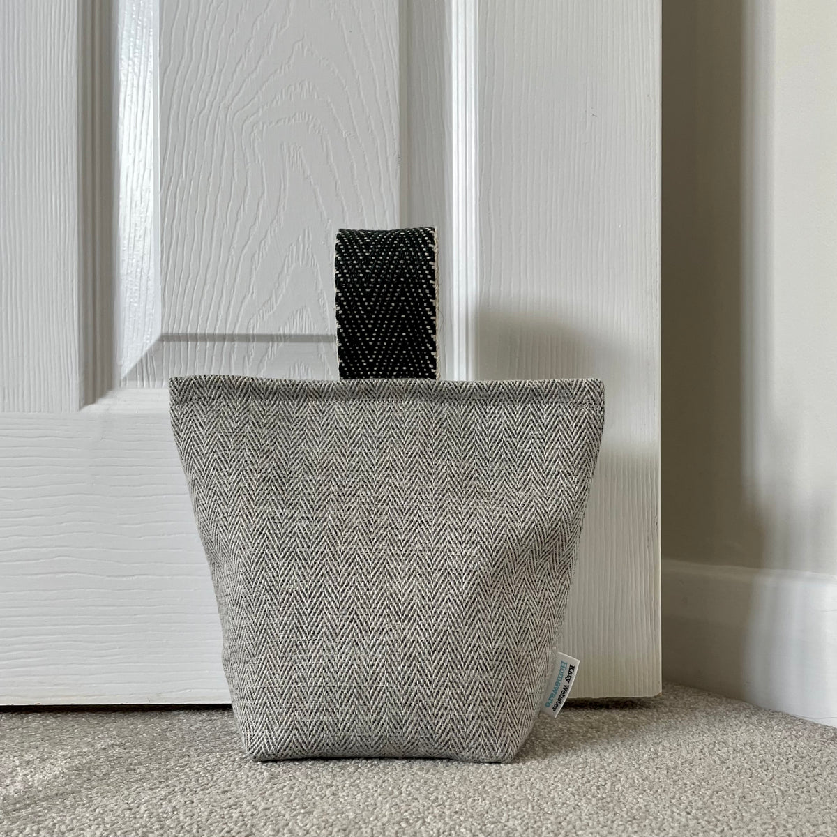 Textured grey herringbone doorstop with black jute handle against a white panelled door.