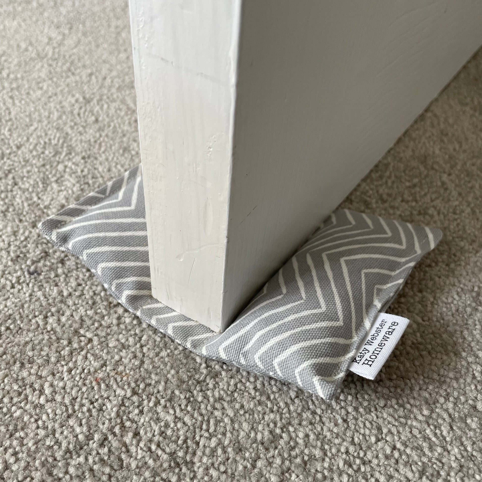 Gray and white striped door stopper on a carpeted floor with a visible brand tag.