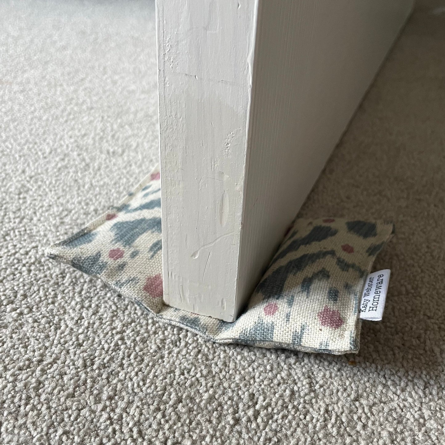 Ikat pattern pale blue and pink door wedge on a carpeted floor