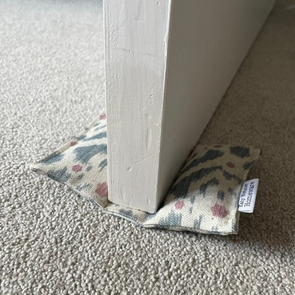 Ikat pattern pale blue and pink door wedge on a carpeted floor