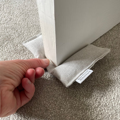 Fabric door stopper with a hand holding it against a white door on a carpeted floor.