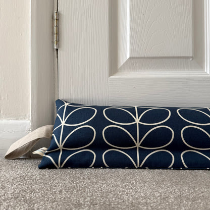 A navy blue fabric draught excluder with a cream geometric leaf pattern, resting on a grey carpet in front of a white panelled door.