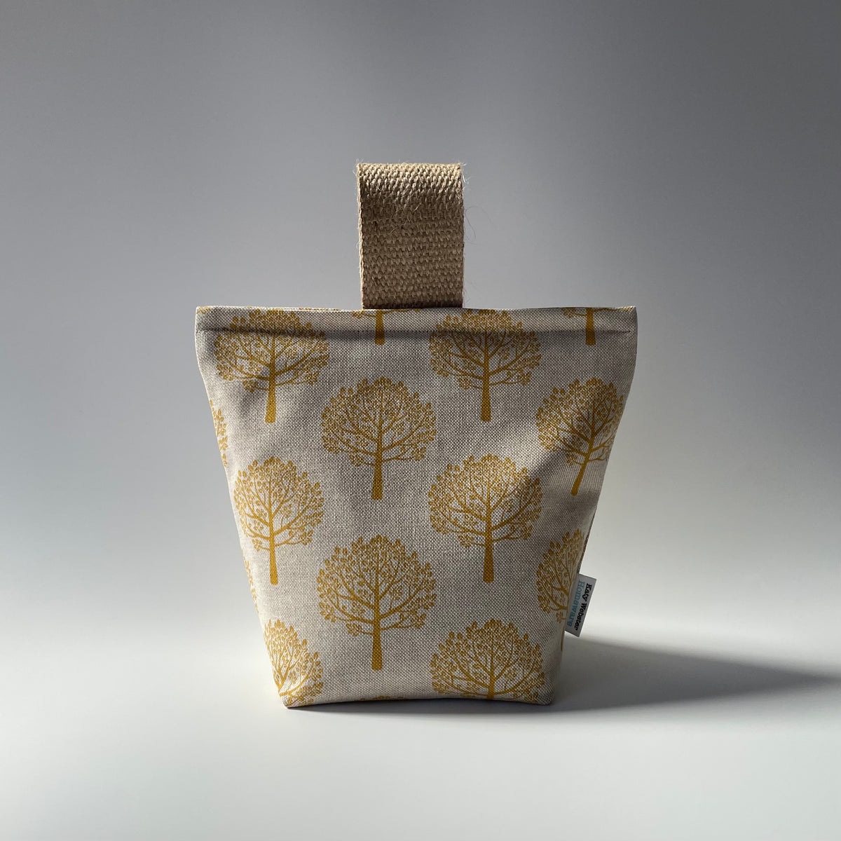 An ochre mulberry fabric doorstop with a jute handle, featuring a botanical print with trees.
