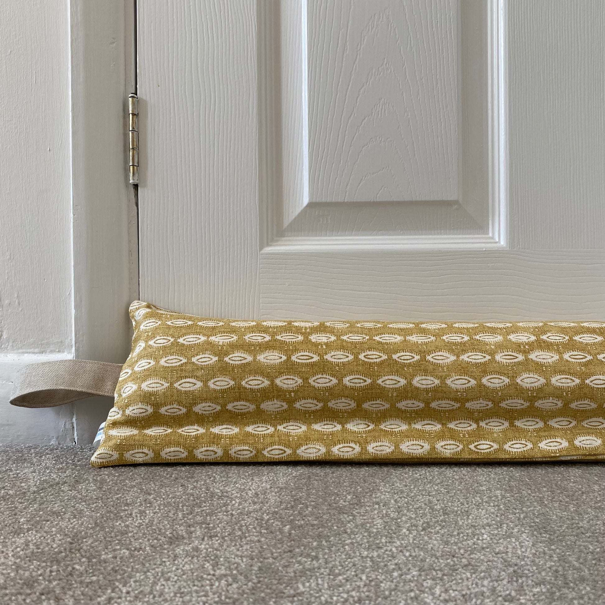 Ochre yellow patterned weighted draught excluder with washable cover and beige hanging loop.