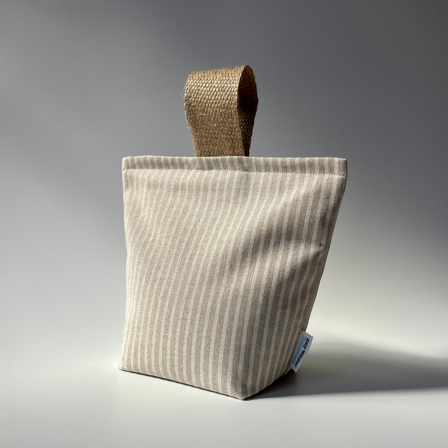 Fabric doorstop with a beige and white vertical pinstripe pattern, featuring a thick jute handle on top.