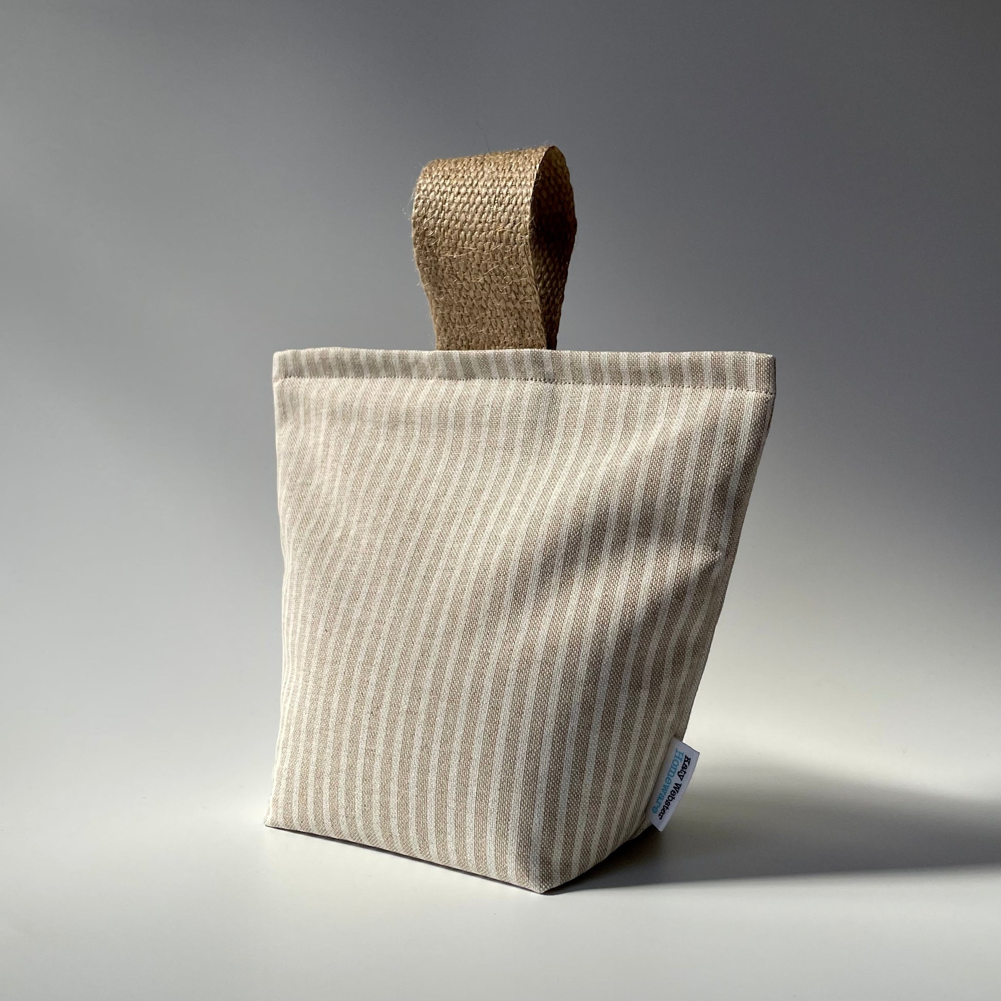Fabric doorstop with a beige and white vertical pinstripe pattern, featuring a thick jute handle on top.