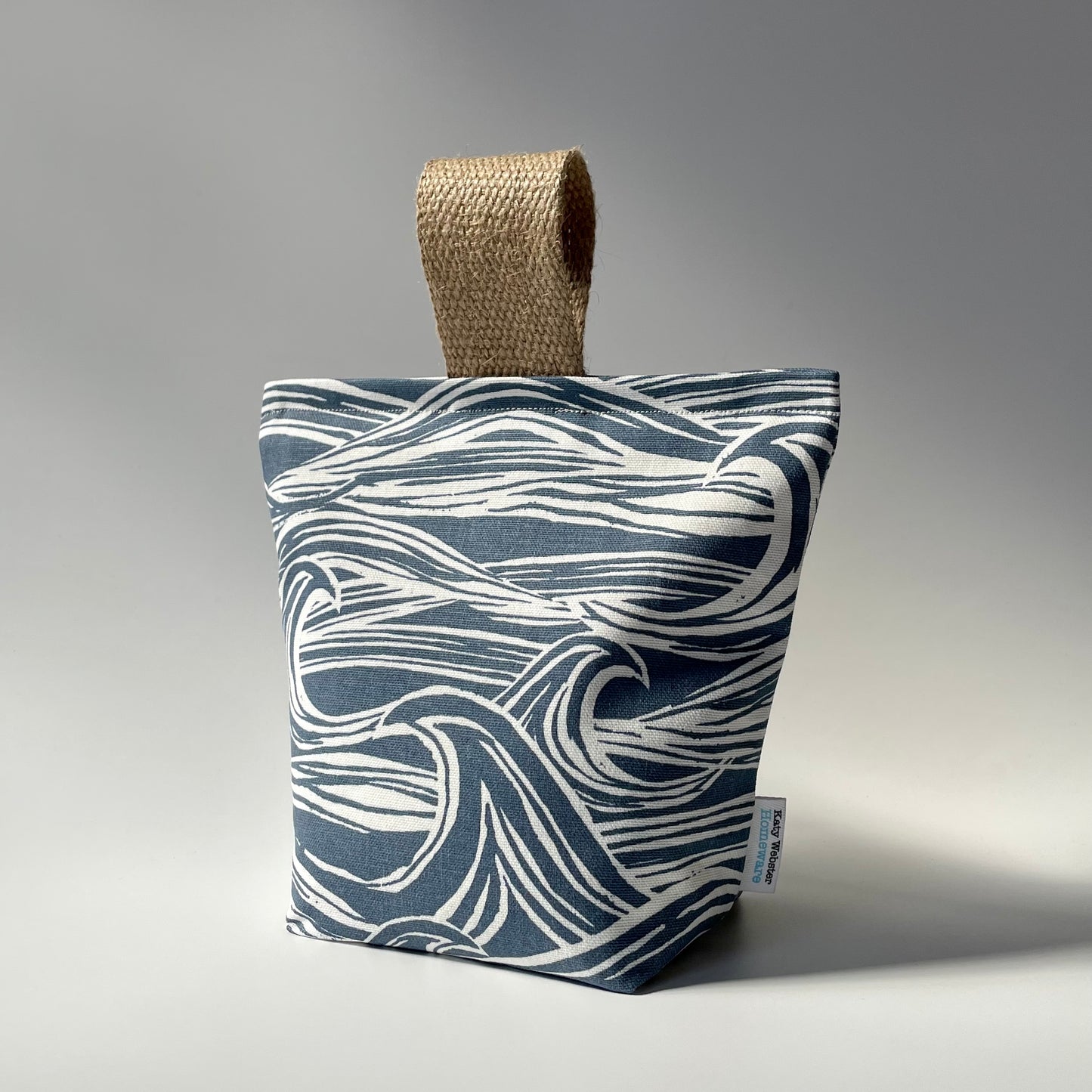 Fabric doorstop with a navy blue and white wave pattern, featuring a thick jute handle on top.
