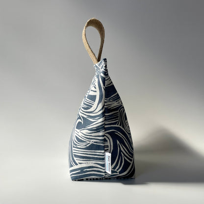 Side profile of fabric doorstop with a navy blue and white wave pattern, featuring a thick jute handle on top.