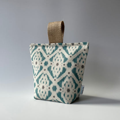 Fabric door stop with a neutral background and teal and grey geometric Ikat pattern with a thick jute handle on top.