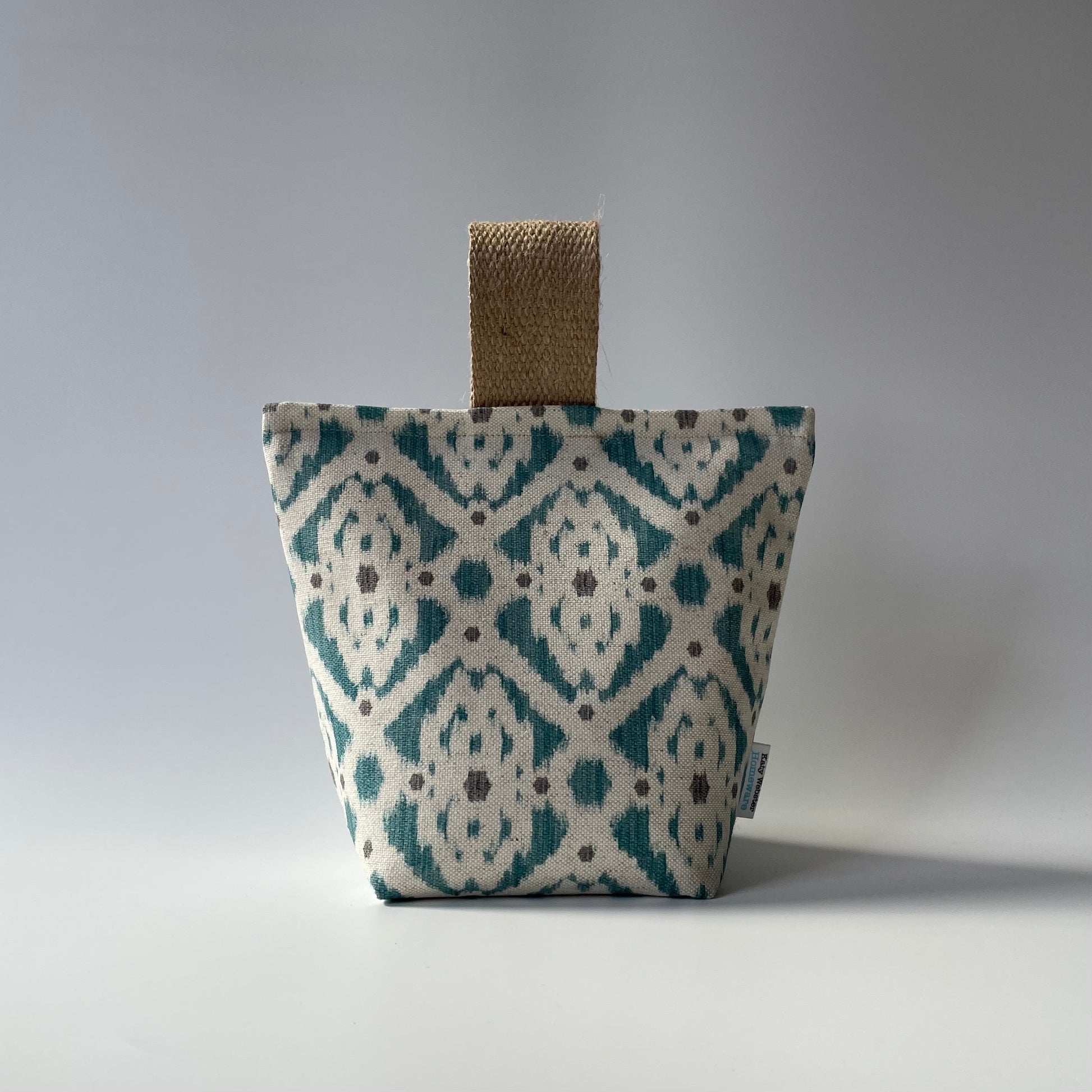 Fabric doorstop with a neutral background and teal and grey geometric Ikat pattern with a thick jute handle on top.