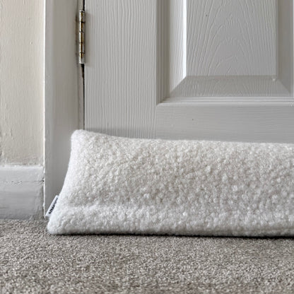 A white textured boucle draught excluder resting on a grey carpet in front of a white paneled door.