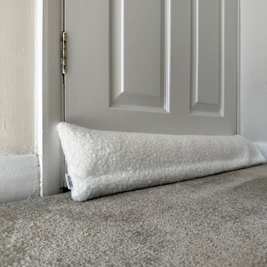 A white boucle draught excluder resting on a grey carpeted floor in front of a white paneled door.