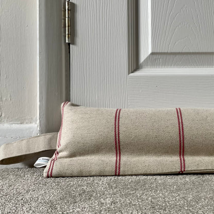 Beige draft excluder with red stripes on a grey carpet placed beneath a white panelled door.