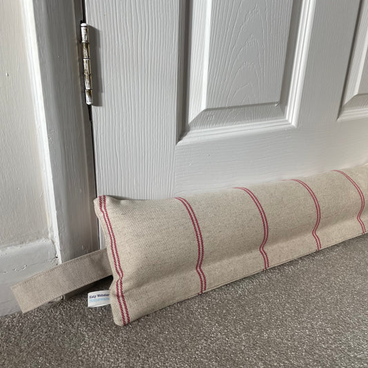 Beige draft excluder with red stripes on a grey carpet placed beneath a white panelled door.