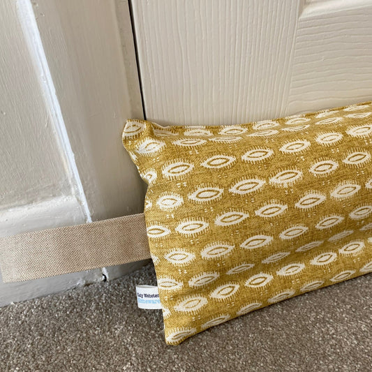 Ochre yellow patterned weighted draught excluder with washable cover and beige hanging loop.