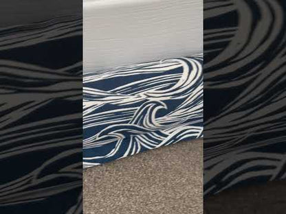 Navy and white wave-patterned draught excluder on a carpet floor next to a closed door.