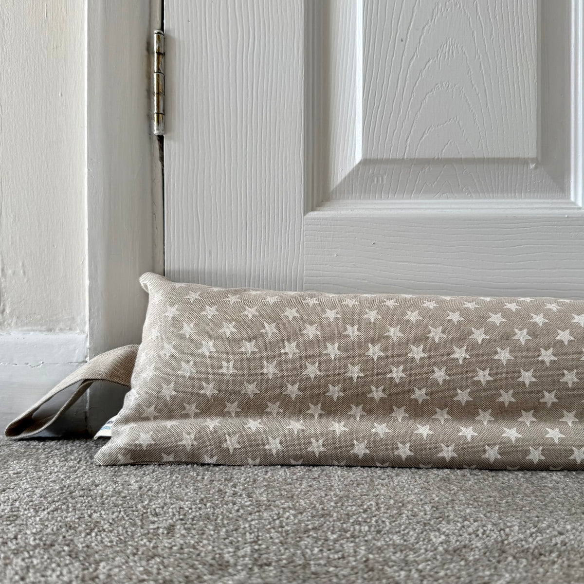 A fabric draught excluder with a beige and white star pattern resting on a grey carpet in front of a white panelled door.