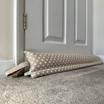 A fabric draught excluder with a beige and white star pattern rests on a carpeted floor in front of a closed panelled door.