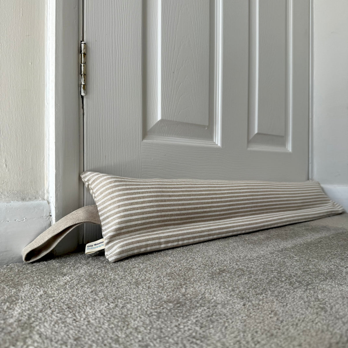 A striped fabric draught excluder resting on a carpeted floor in front of a white paneled door.